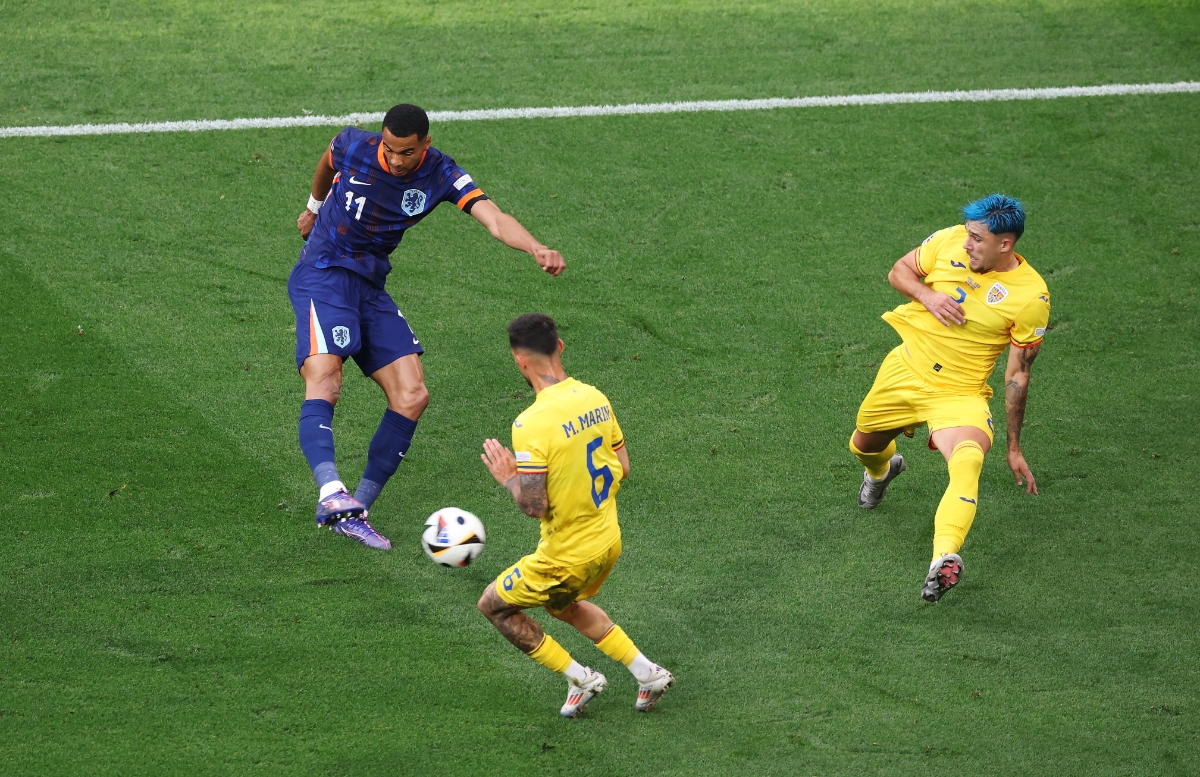 Cody Gakpo of the Netherlands scores his team's first goal whilst under pressure from Marius Marin and Andrei Ratiu of Romania during the UEFA EURO 2024 round of 16 match between Romania and Netherlands at Munich Football Arena.