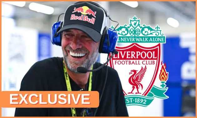 Jurgen Klopp smiles whilst wearing a Red Bull hat and headphones with a Liverpool club crest in the background.