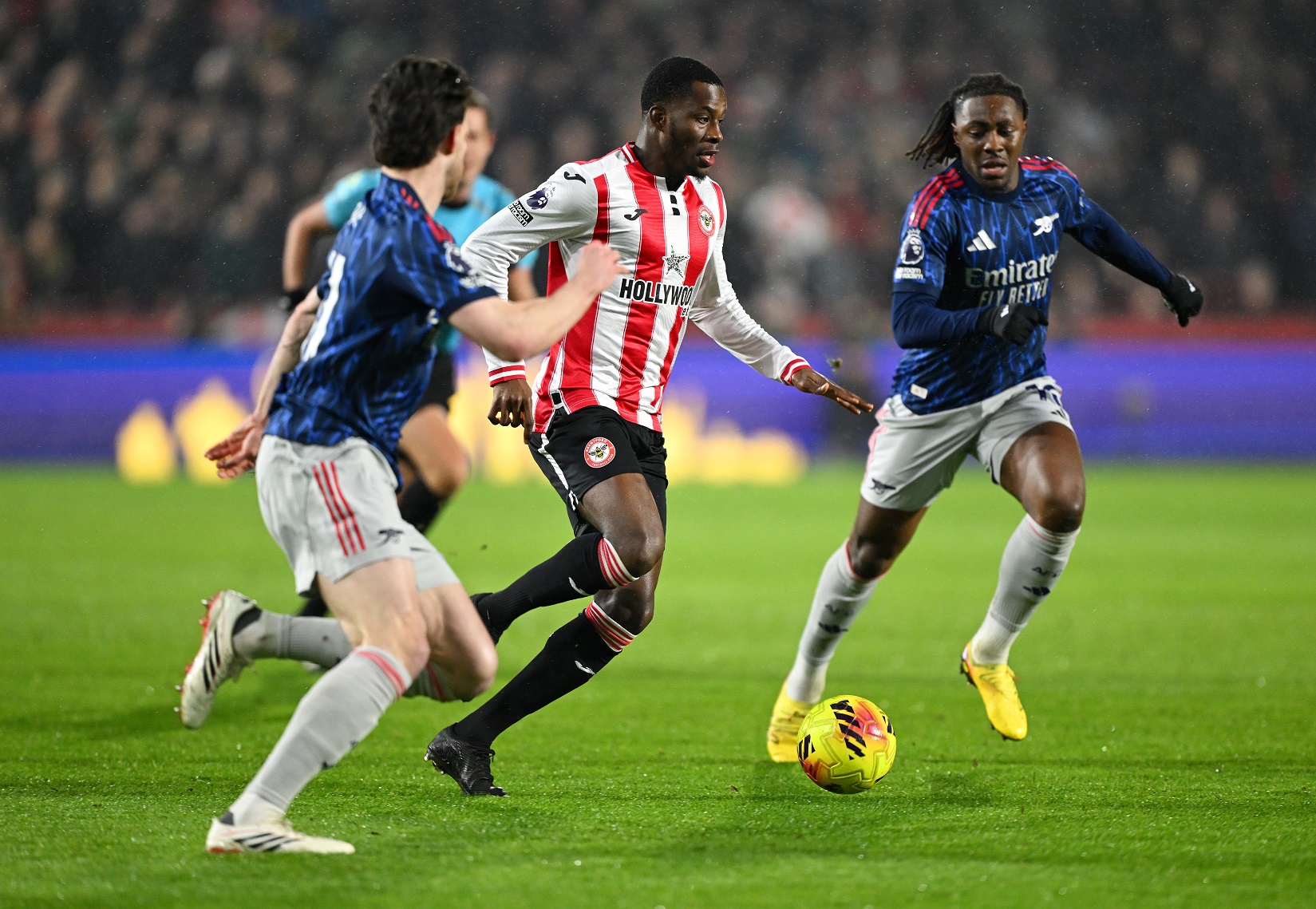 Dango Ouattara of Brentford runs with the ball whilst under pressure from Declan Rice and Eberechi Eze of Arsenal