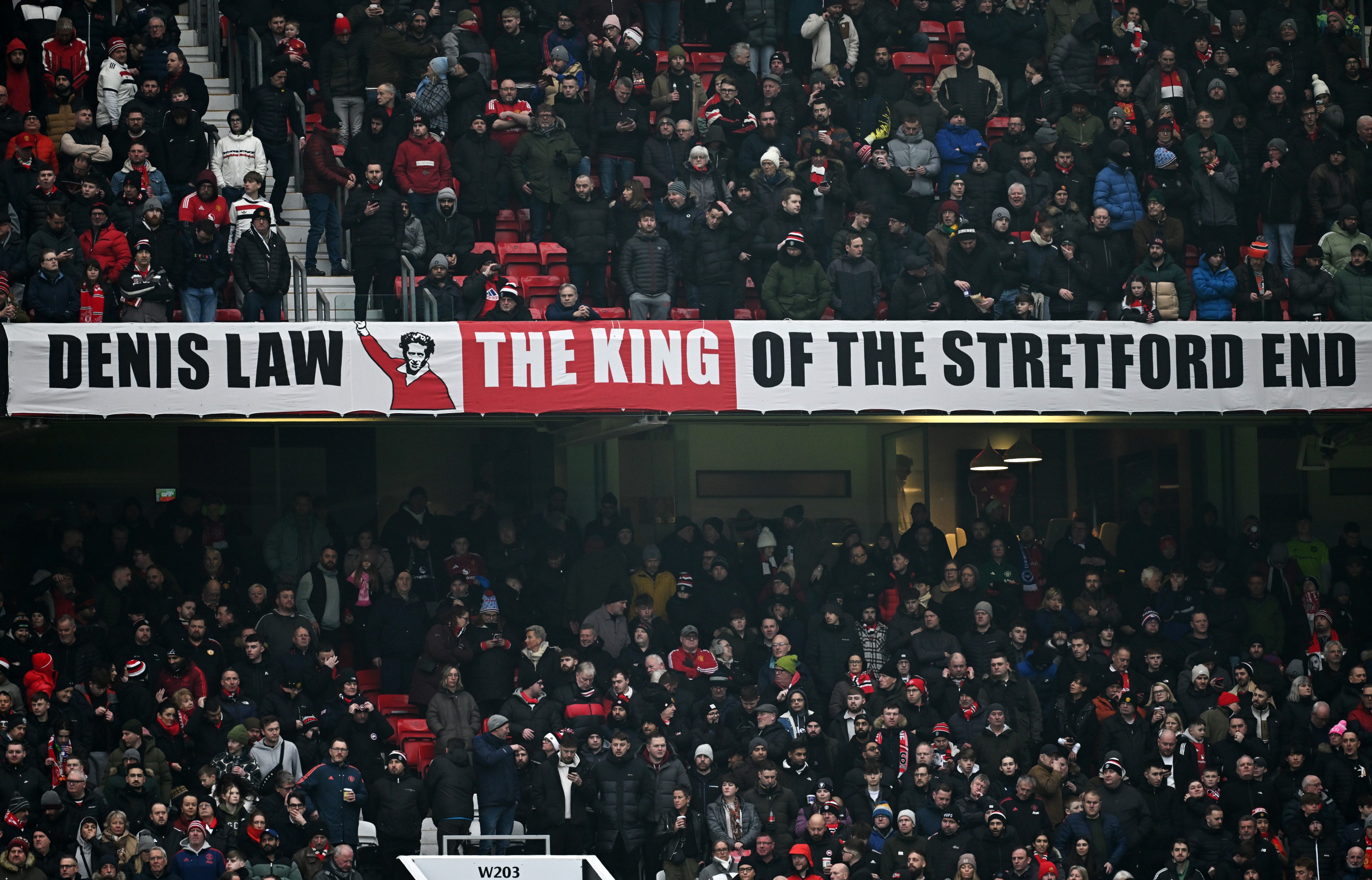 A banner which reads 'Denis Law, The King of the Stretford End' is seen inside the stadium