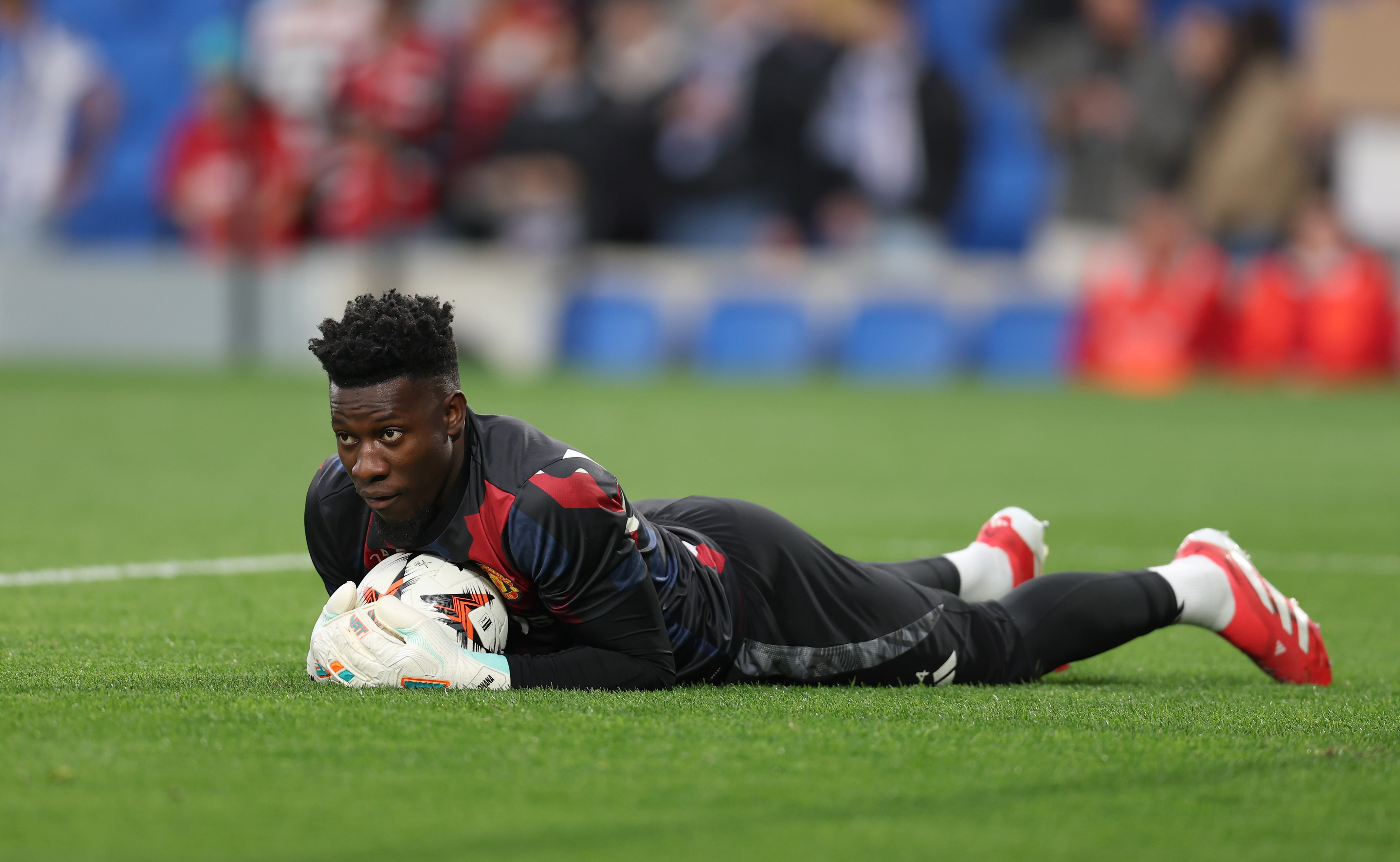 Andre Onana lies down and clutches the ball on the ground.