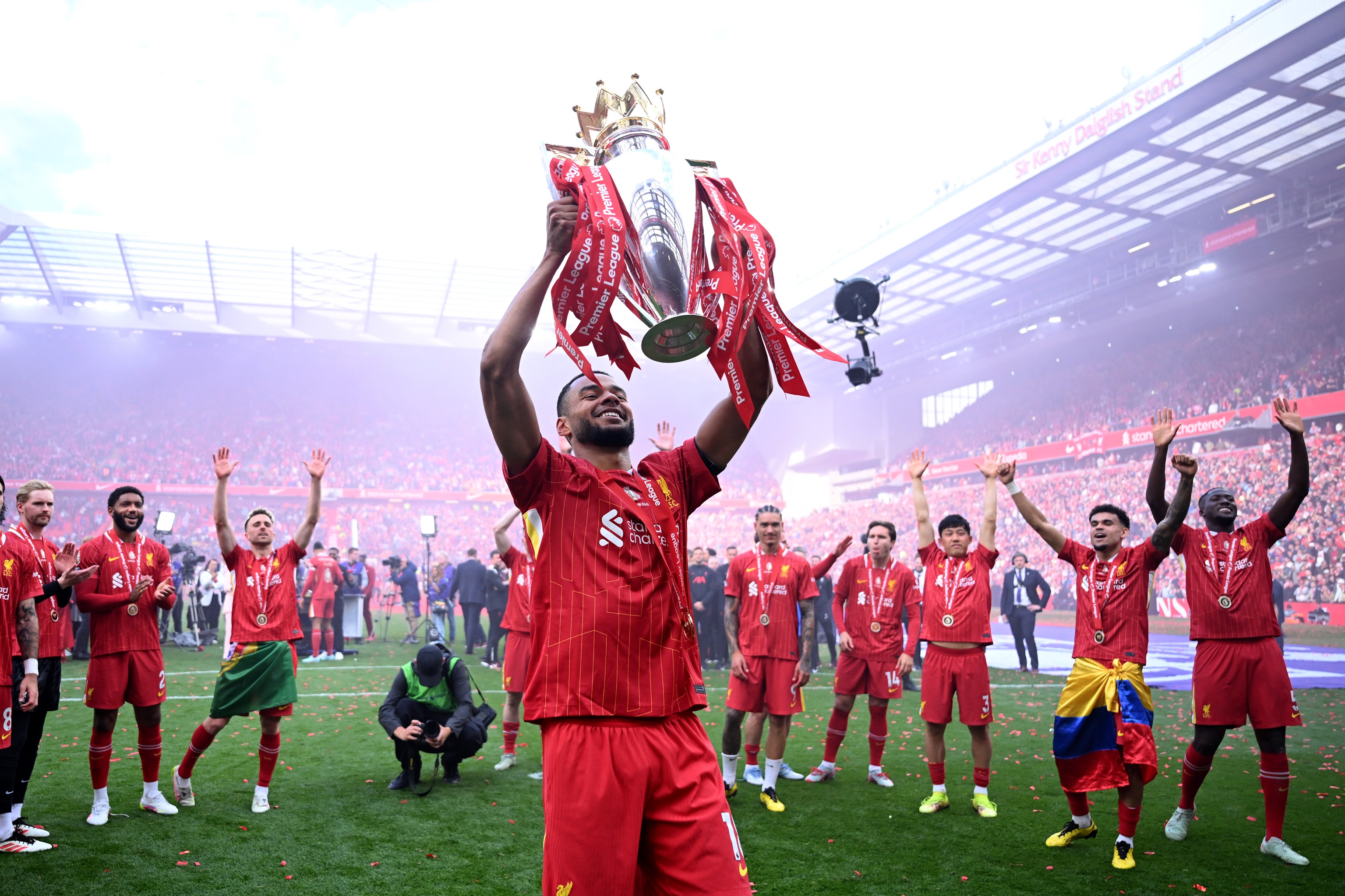 Cody Gakpo lifts the Premier League trophy in front of Luis Diaz and Liverpool fans at Anfield.