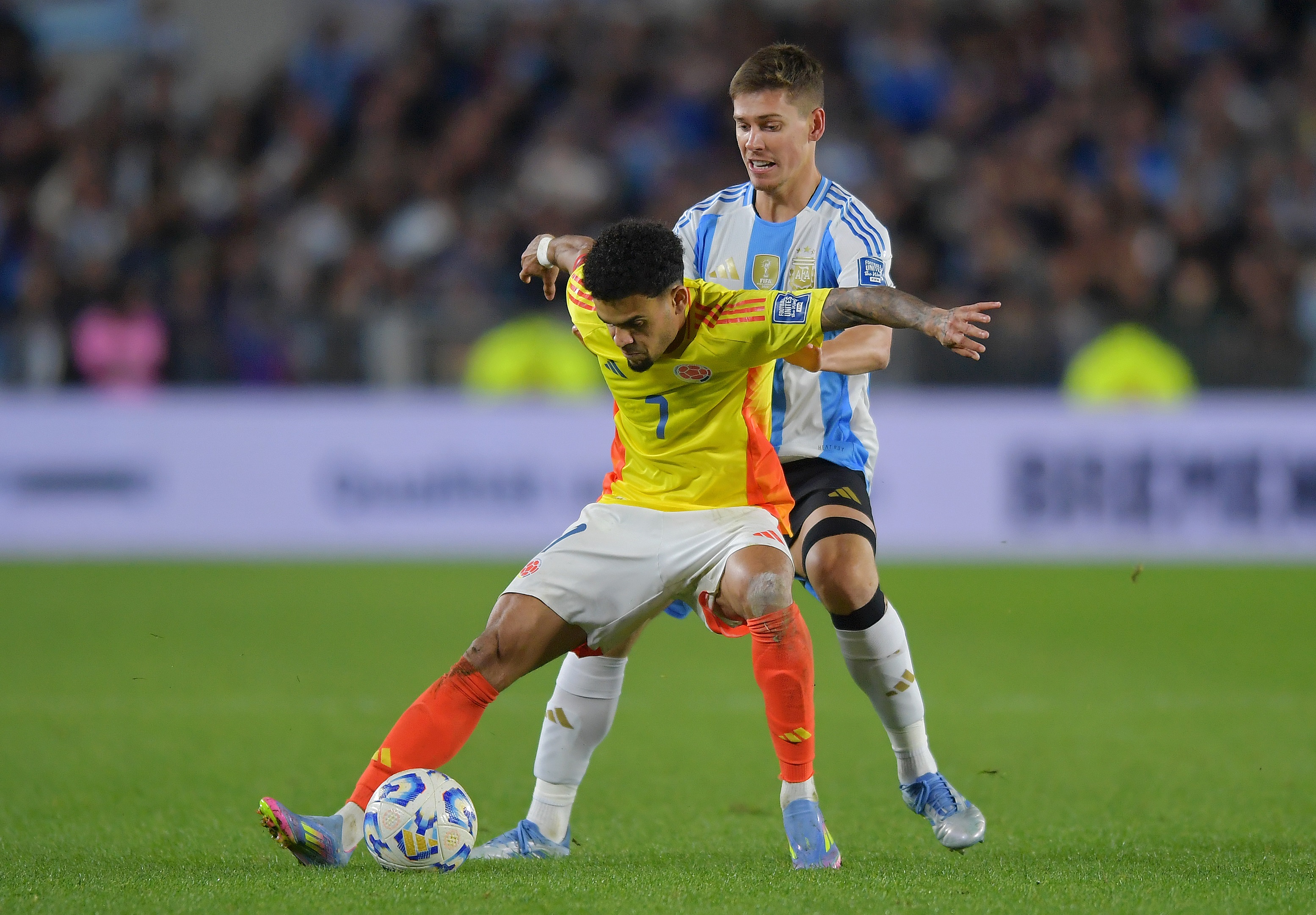 Luis Diaz holds off an Argentina player away from the ball.