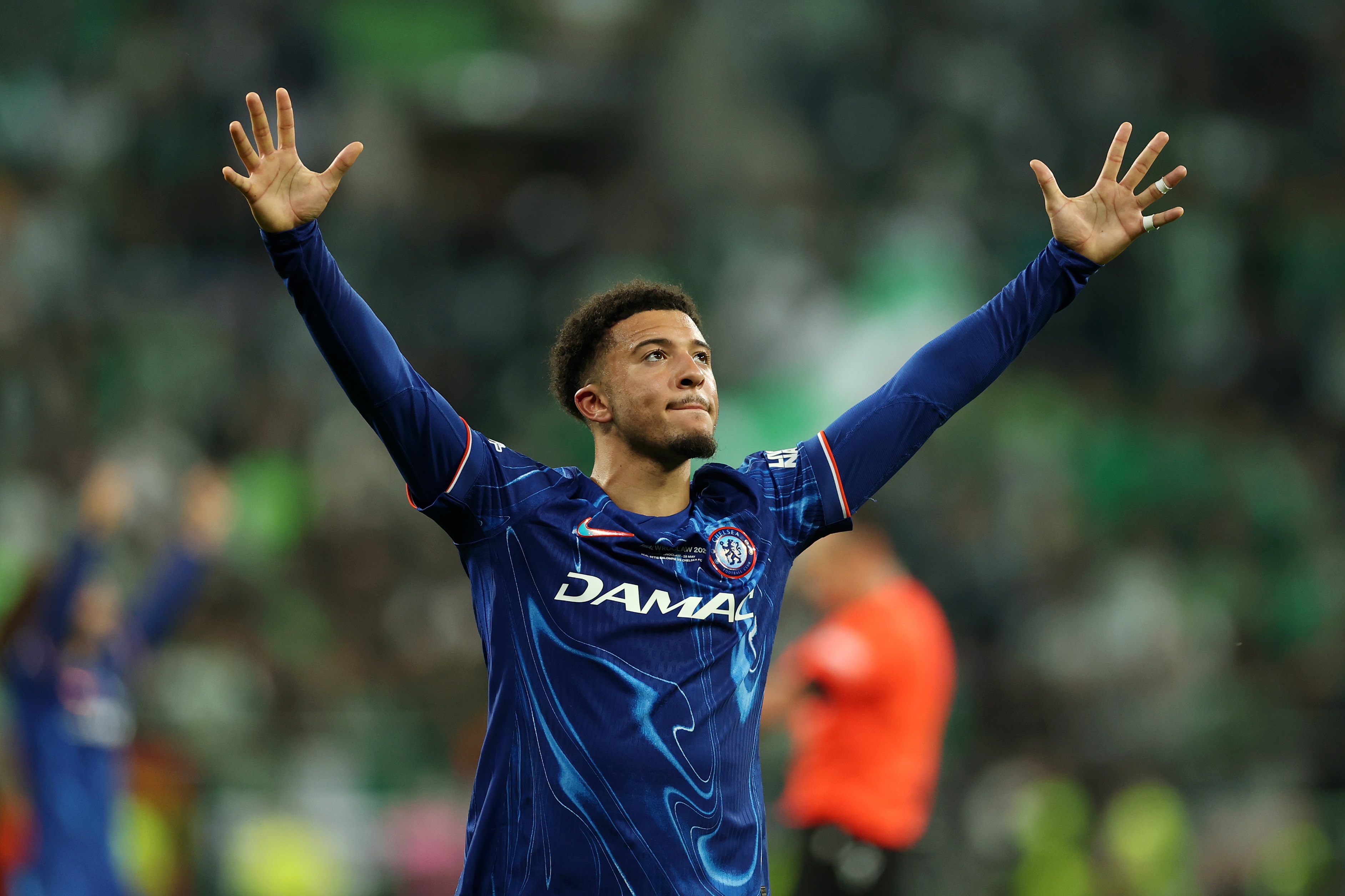 Jadon Sancho holds his arms up wide in the air.